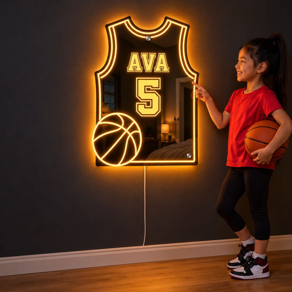 A young basketball player holding her ball and pointing at her lit jersey mirror on the wall