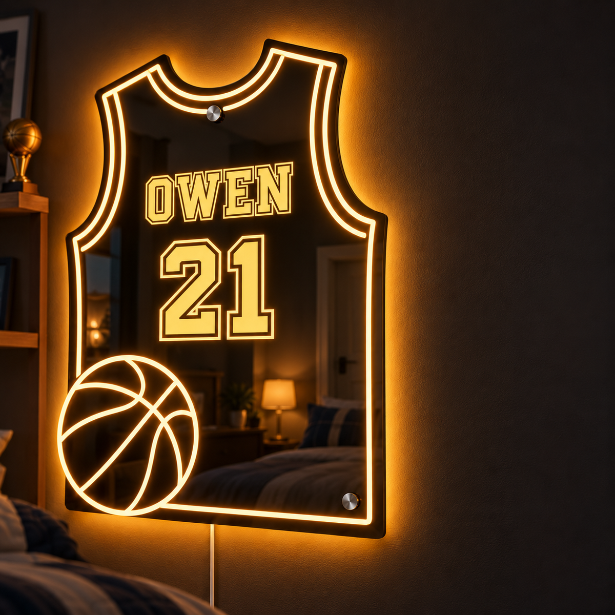 Close-up of the jersey-shaped LED mirror lit amber on a dark bedroom wall, engraved with the name OWEN and the number 21