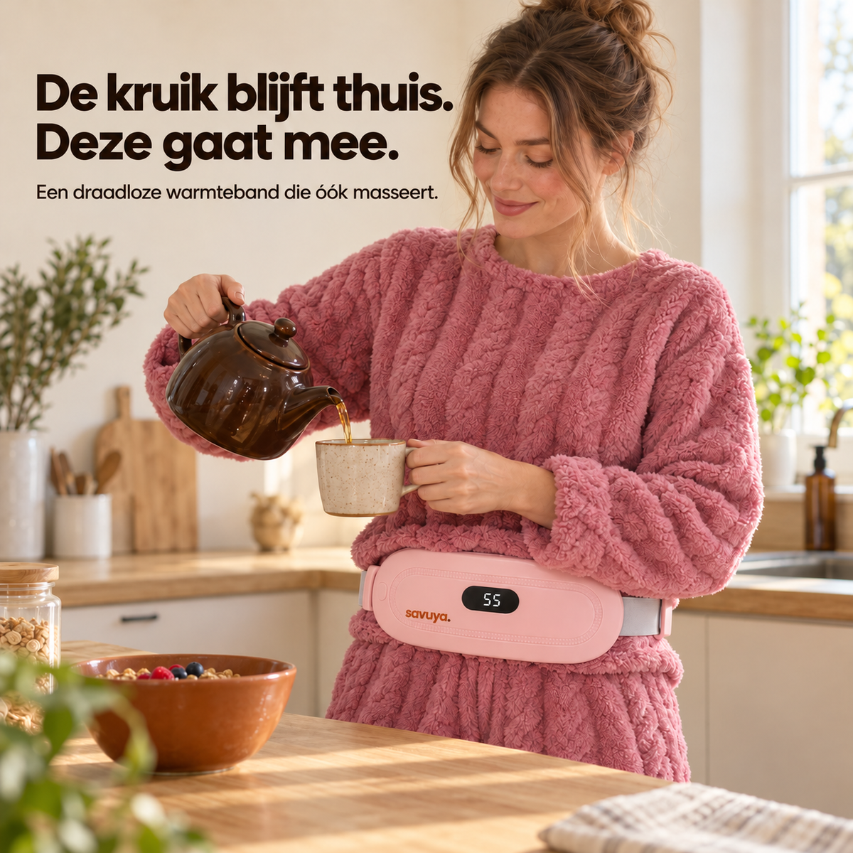 Vrouw in de keuken schenkt thee in, met de roze warmteband om haar middel; op het display staat 55